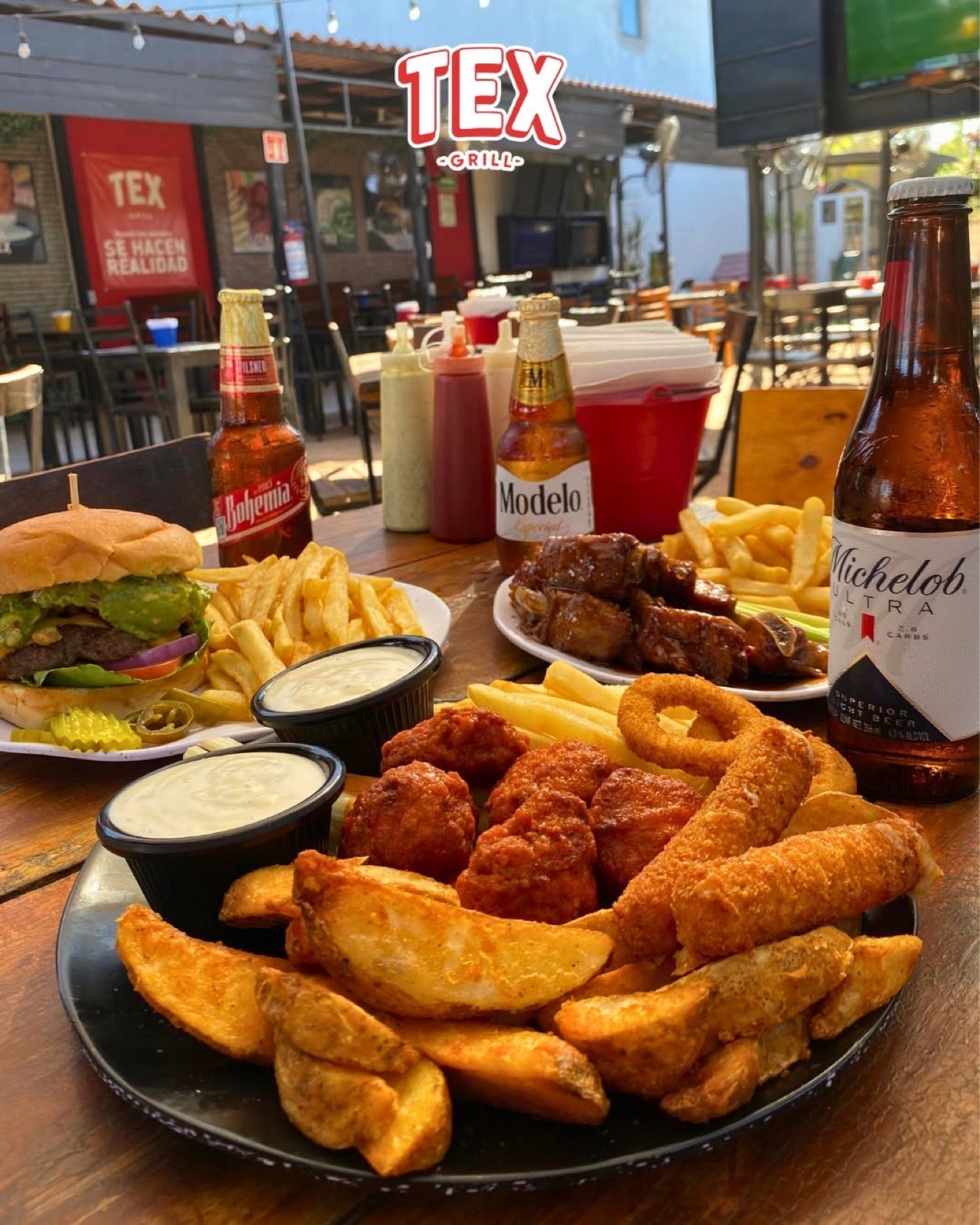 Mesa con hamburguesa, botana y cervezas en la terraza de Tex Grill Los Mochis